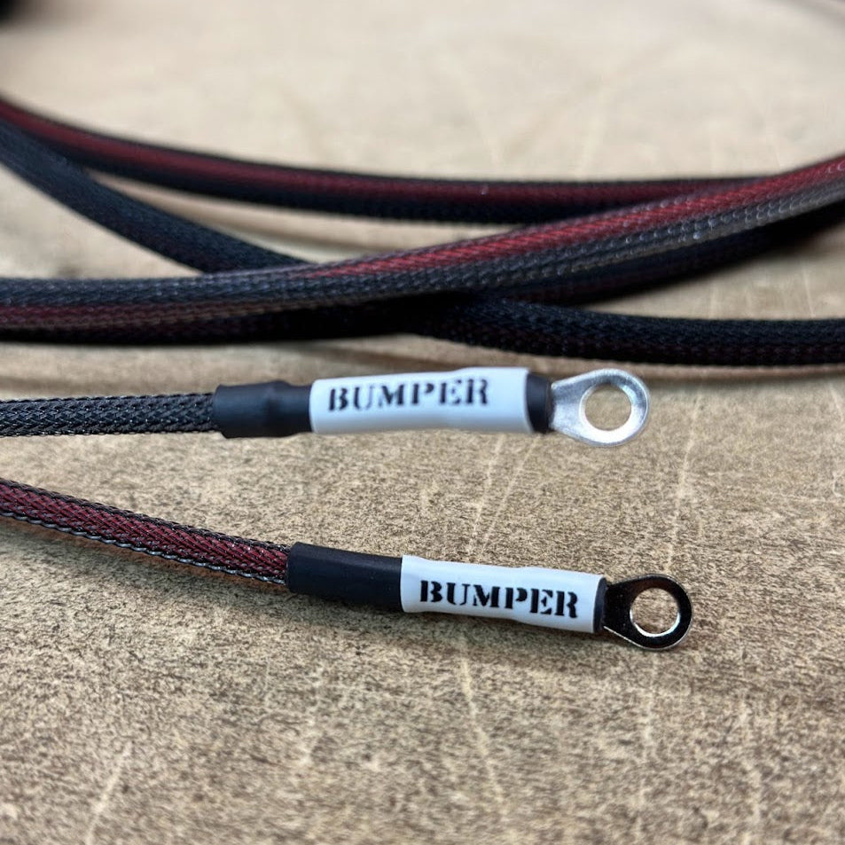 Close-up of a black and red vehicle wiring harness with 'BUMPER' text printed on it, lying on a metallic surface.
